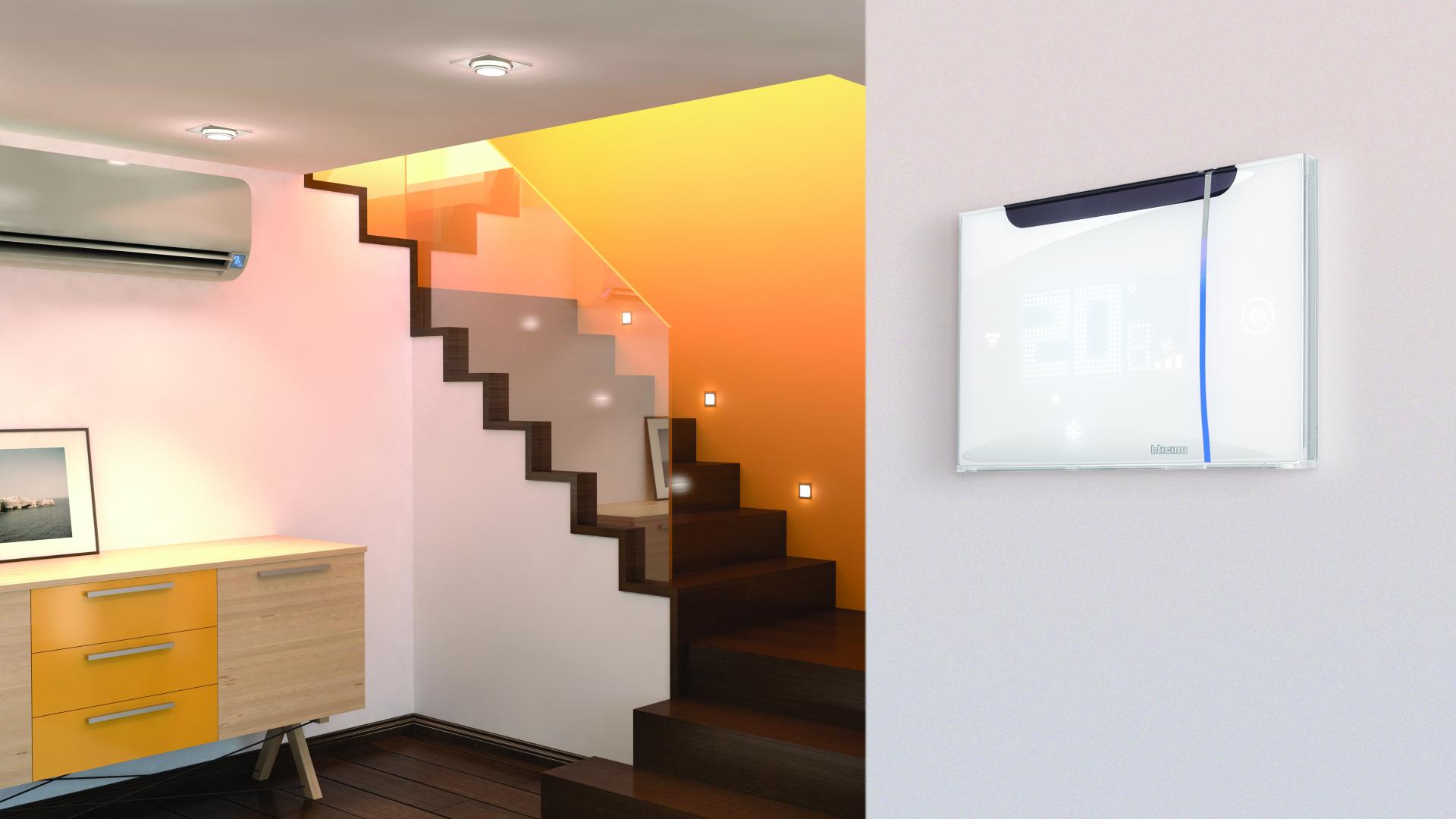 Interni moderni con scale in legno, aria condizionata e un termostato Smarther AC with Netatmo montato a parete.